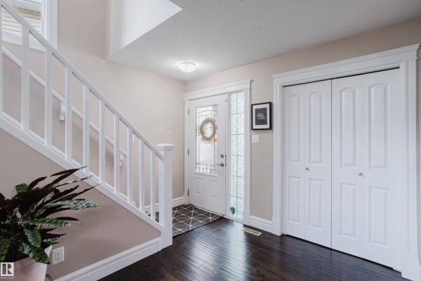 Interior entryway with dark hardwood floors, white staircase, double white doors, and glass front door. - 12207 171 Av Nw, Edmonton