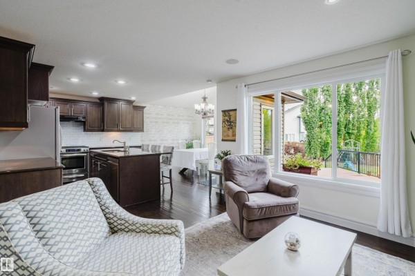 Living room and kitchen area with dark cabinets, white backsplash, large window, and seating. - 12207 171 Av Nw, Edmonton