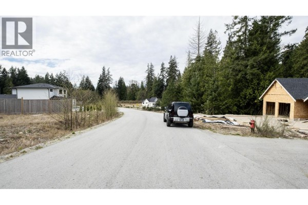 A quiet road winds through a developing area with surrounding trees and property lines. - 1221 Castle Road, Gibsons
