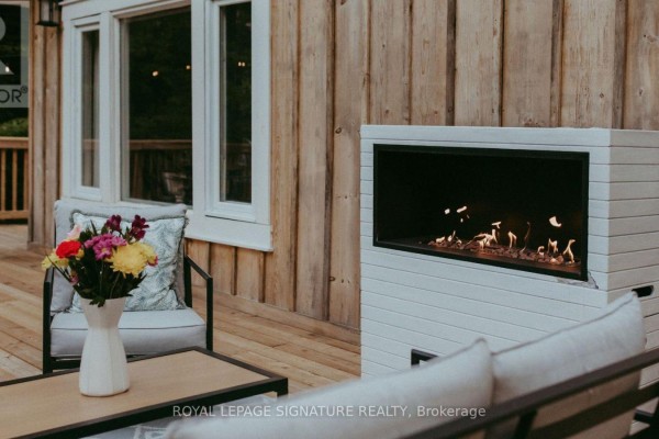 Close-up of a modern outdoor gas fireplace on a wooden deck with floral arrangement. - 1221 Hand Drive, Highlands East