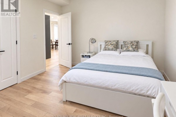 Bedroom with a white queen bed, blue throw blanket, bedside table, and light wood flooring. - 1221 Meadowlands Drive E, Ottawa