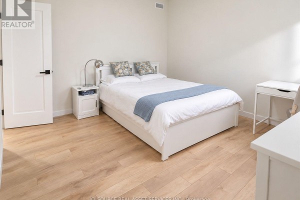 Bedroom with a white queen bed, bedside table, small desk, and light wood flooring. - 1221 Meadowlands Drive E, Ottawa