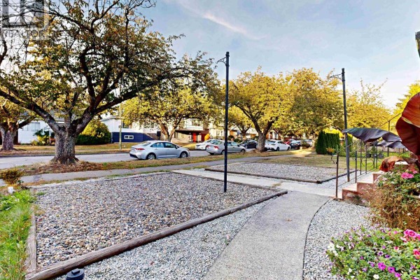 Sidewalk leading past gravel yards and trees towards a street with parked cars. - 1222 E 51st Avenue, Vancouver