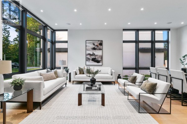 Spacious living room with white sofas, black framed windows, and glass coffee table. - 1222 Mississauga Road, Mississauga