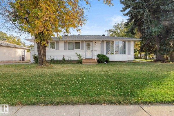 Street-level view of the white bungalow's entrance with a lawn and mature trees in the front yard. - 12227 58 St Nw, Edmonton