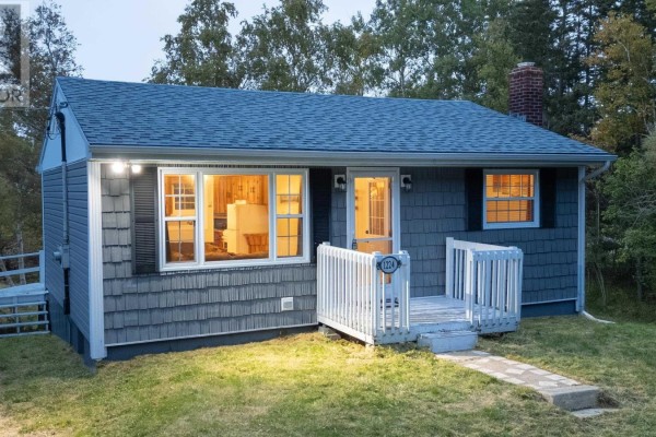 Close-up front view of a grey vinyl-sided bungalow with lighted windows and a white front porch. - 1224 Georges River Rd Road, Georges River