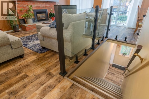 Living room with fireplace, sofa, and glass-paneled stairs leading down to a hallway. - 1224 Third Avenue, Trail