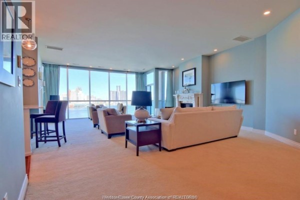 Living room with plush carpet, light blue walls, a fireplace, and a large window view. - 1225 Riverside Dr. Unit# 1204, Windsor