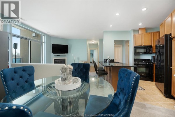 Glass dining table with blue chairs, fireplace, TV, and kitchen island - 1225 Riverside Unit# 409 Windsor