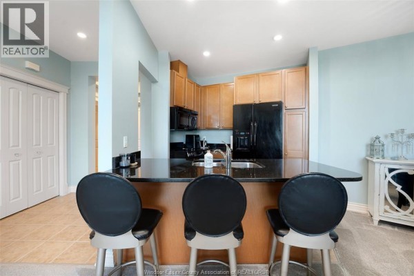 Kitchen with breakfast bar, granite counters, wood cabinets, and black appliances - 1225 Riverside Unit# 409 Windsor
