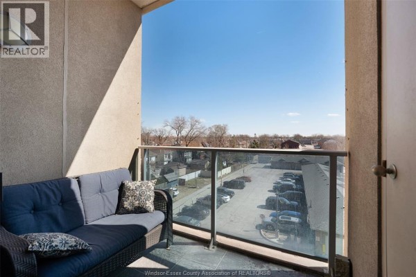 Balcony with wicker sofa and glass railing overlooking a parking lot and neighborhood. - 1225 Riverside Unit# 409 Windsor