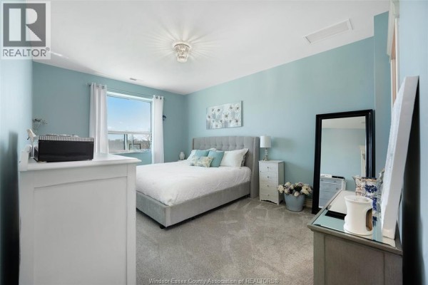 Bedroom with upholstered bed, mirror, and light blue walls - 1225 Riverside Unit# 409 Windsor
