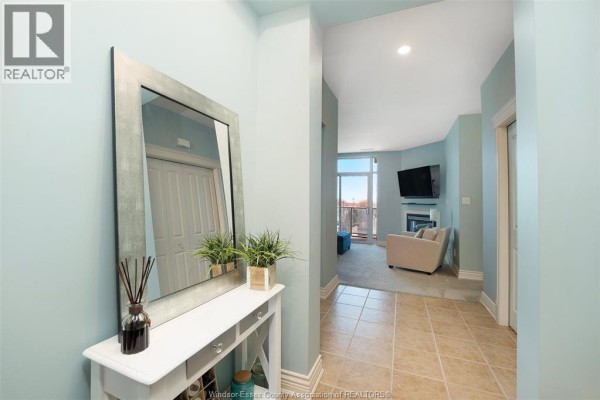 Hallway with console table, mirror, leading to living room with fireplace, TV, and balcony. - 1225 Riverside Unit# 409 Windsor