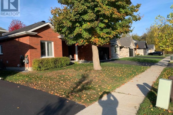 Side view of a red brick bungalow with a manicured lawn and a tree in the driveway. - 1228 Innwood Avenue, Cornwall