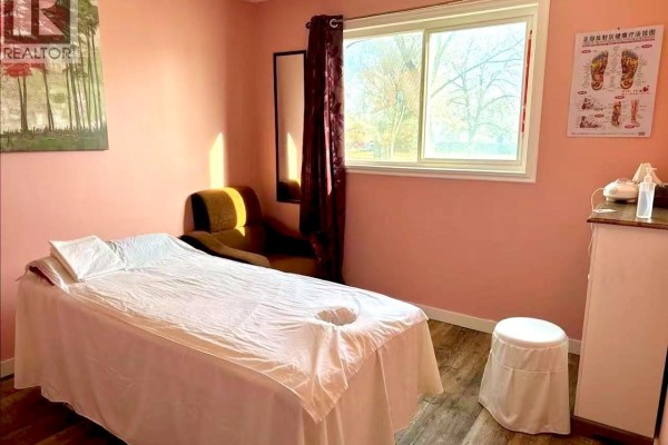 Reception area with a beige sofa, a wooden reception desk, and framed artwork on the wall. - 1229 Idylwyld Drive N, Saskatoon