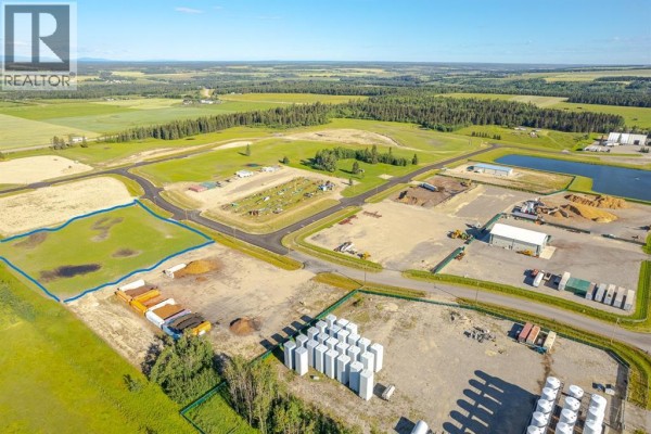Aerial view of a developed area with buildings, storage containers, and a large field outlined. - 123, 32532 Range Road 42, Rural Mountain View County