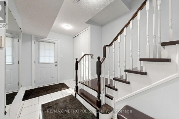 Interior view of a bright hallway with white tiled floor, white stairs, and dark wood banister. - 123 - 2 Hedge End Road, Toronto