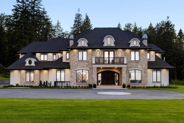Wide shot of a large stone and cream-colored home with forest backdrop. - 123 208 Street, Langley