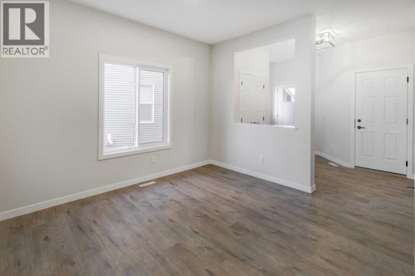 Empty living room with light grey walls, a white window, and wood-look laminate flooring. - 123 Homestead Circle Ne, Calgary