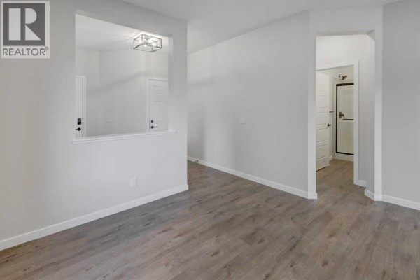 Interior view of an empty room with light grey walls and wood-look laminate flooring, showing a doorway to a bathroom. - 123 Homestead Circle Ne, Calgary
