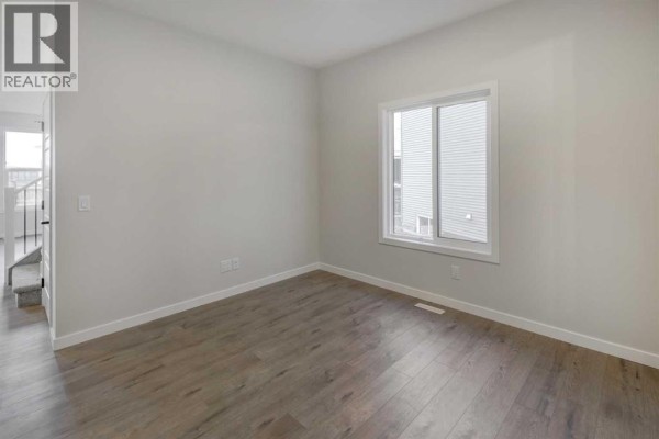 Empty room with light grey walls, a white window, and wood-look laminate flooring, with a view of the entryway stairs. - 123 Homestead Circle Ne, Calgary