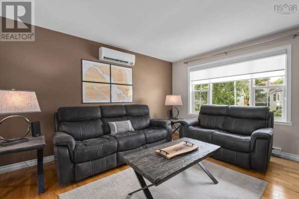 Living room with charcoal couches, coffee table, and large window overlooking greenery. - 123 Lancaster Drive, Dartmouth