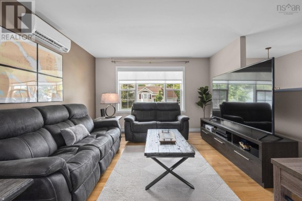 Living room with charcoal couches, large window, TV console, and wooden floors. - 123 Lancaster Drive, Dartmouth