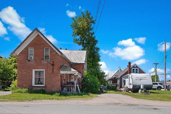 The front and side of a two-story brick house with a weathered porch and snow-covered ground. - 123 Rue Centre, Shawville