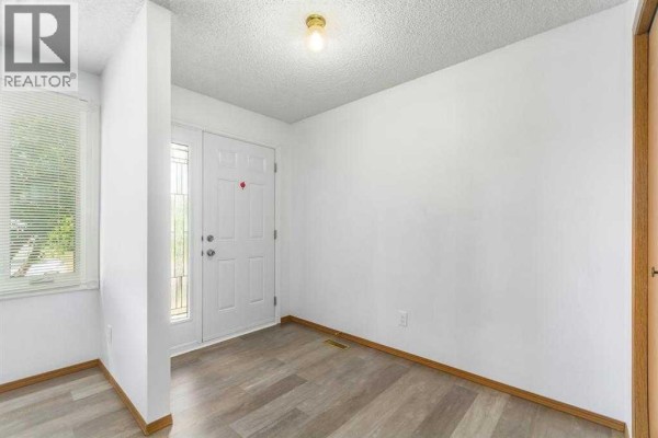 Interior entrance hall with white walls, a white front door, and wood-look laminate flooring. - 123 Whitworth Way Ne, Calgary