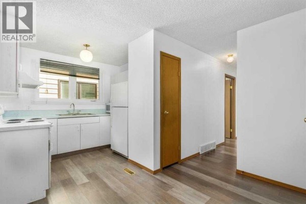 Kitchen with white cabinets and appliances, stainless steel sink, and laminate flooring. - 123 Whitworth Way Ne, Calgary