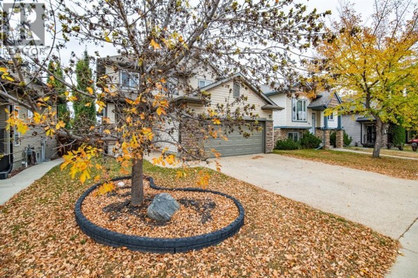 Front exterior of a beige two-story house with a stone-accented garage and entrance during autumn. - 123 Wiley Crescent, Red Deer