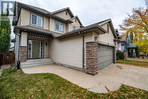 Side exterior of a beige two-story house with a stone-accented garage and entrance, showing Christmas lights. - 123 Wiley Crescent, Red Deer