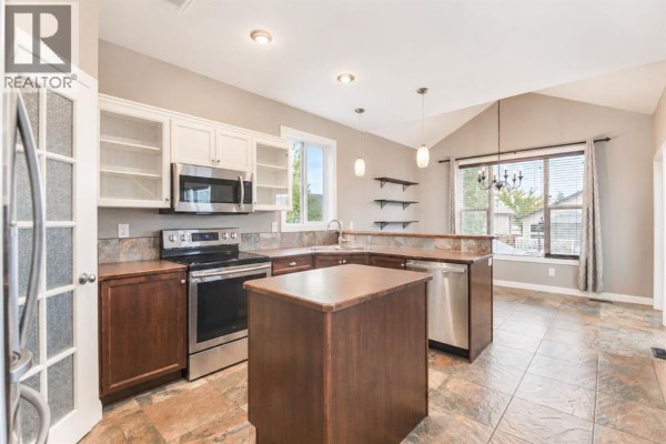 Kitchen with stainless steel appliances, white and wood cabinets, island, and adjacent dining area. - 123 Wiley Crescent, Red Deer