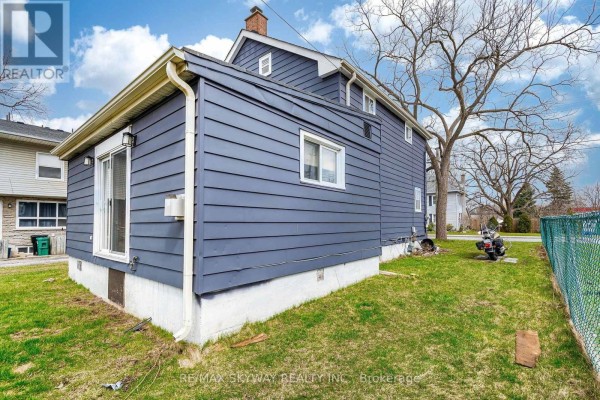 Corner view of the blue house showing the foundation and backyard with a green fence. - 1230 Duke Street, Cambridge