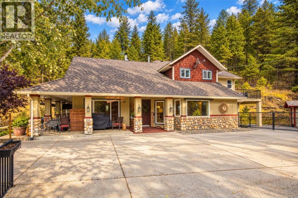 Front exterior of a large house with stone accents and a covered porch, surrounded by trees. - 12300 Highway 33 E Highway E, Kelowna
