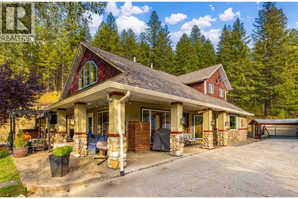 Side exterior view of the house showing a covered porch, stone pillars, and attached garage. - 12300 Highway 33 E Highway E, Kelowna