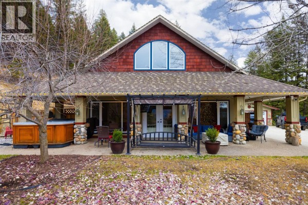 Front view of the house with a wide covered porch, hot tub, and porch swing. - 12300 Highway 33 E Highway E, Kelowna