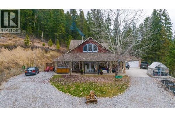 Aerial view of the residential property showing the house, garage, greenhouse, and wooded surroundings. - 12300 Highway 33 E Highway E, Kelowna