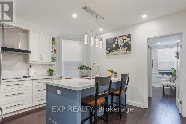 Kitchen with white cabinets, a blue island with pendant lights, and a doorway. - 1231 Bathurst Street, Toronto