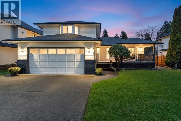 Front exterior of house with double garage and porch, green lawn, and clear sky. - 12329 Bonson Road, Pitt Meadows