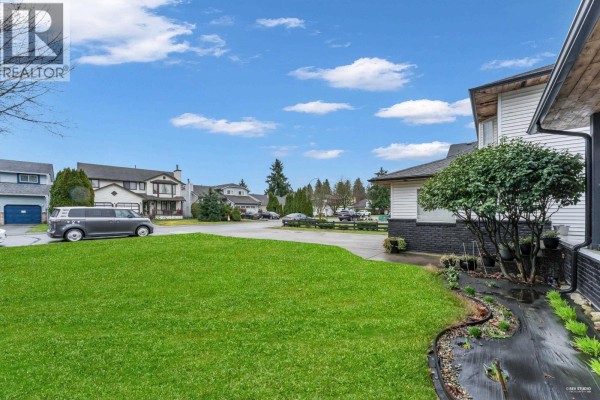 Side view of property showing double garage and spacious driveway on a sunny day. - 12329 Bonson Road, Pitt Meadows