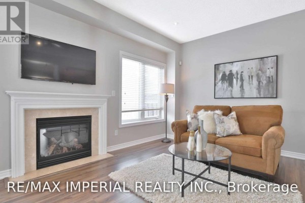 Living room with a tan sofa, fireplace, large windows, and dark wood floors. - 1233 Agram Drive, Oakville