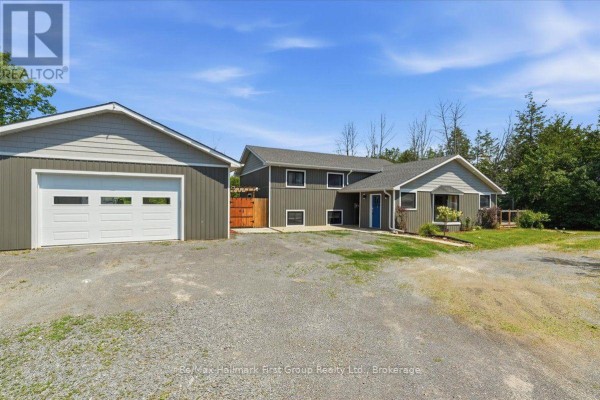 Front view of a two-story grey house with a white garage door and mature trees in the background. - 1233 Lazier Road, Tyendinaga