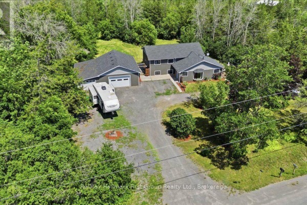 Elevated aerial view of a grey house and garage surrounded by lush green trees and landscaping. - 1233 Lazier Road, Tyendinaga