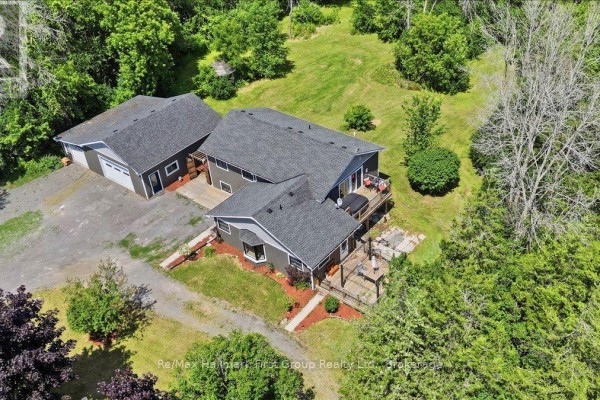 Aerial view of the property showcasing the grey house, garage, decks, and surrounding wooded area. - 1233 Lazier Road, Tyendinaga