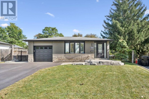 Front exterior of bungalow with grey siding, stone accent wall, garage, and landscaped front yard. - 1233 Michael Crescent, Cambridge