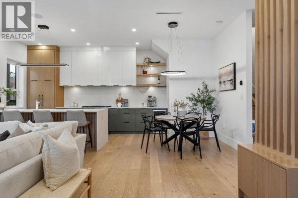Living room and kitchen with white sectional, concrete fireplace surround, and island seating. - 1234 E 19th Avenue, Vancouver