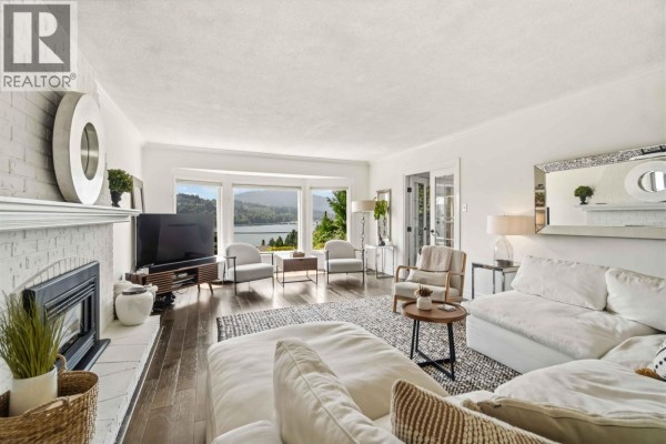 Living room with white sectional sofa, white brick fireplace, dark hardwood floors, and a patterned area rug. - 1237 Ioco Road, Port Moody