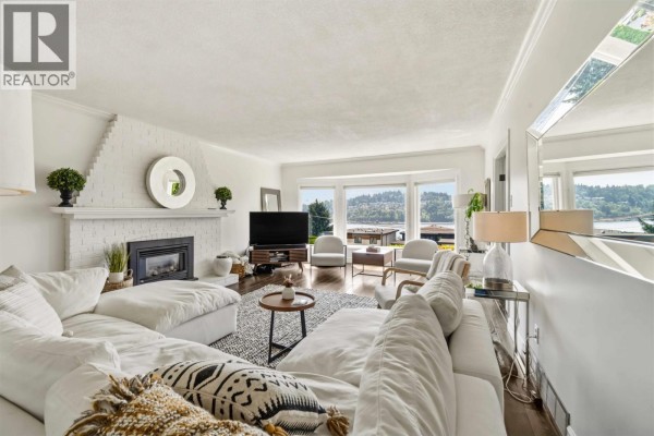 Living room with bay windows overlooking a water view, white sofas, fireplace, and dark hardwood floors. - 1237 Ioco Road, Port Moody