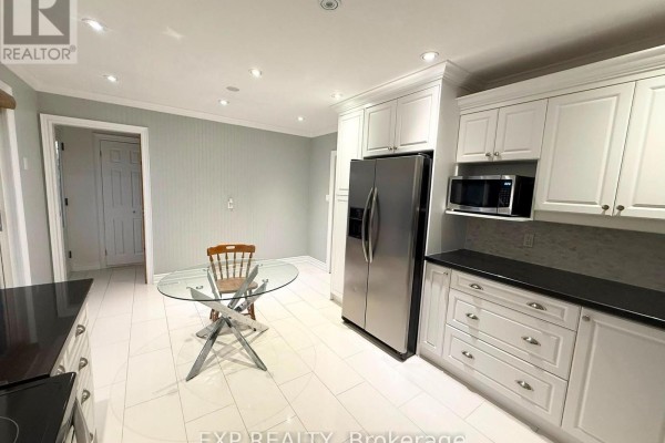Kitchen with white cabinetry, stainless steel refrigerator, microwave, and a glass-top dining table. - 12376 Tenth Line, Whitchurch Stouffville
